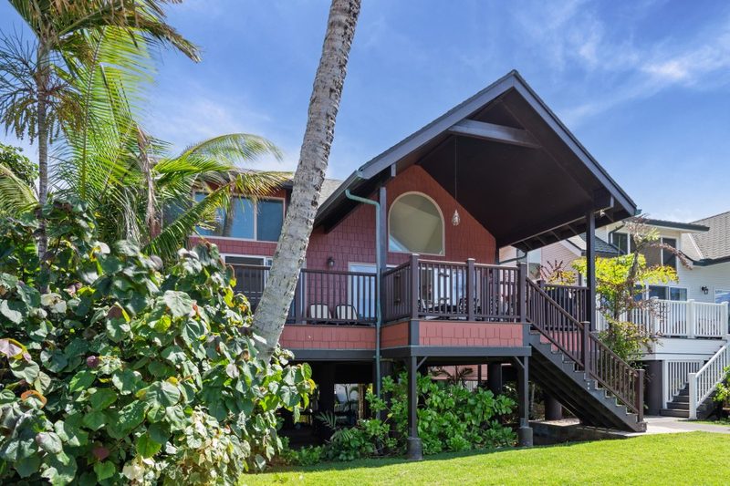 Ginger House, a red timber beach house on stilts with a wide deck, framed by palms